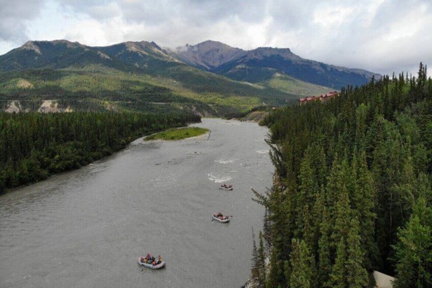 A river with three boats, surrounded by dense forest and mountains in the background. 3