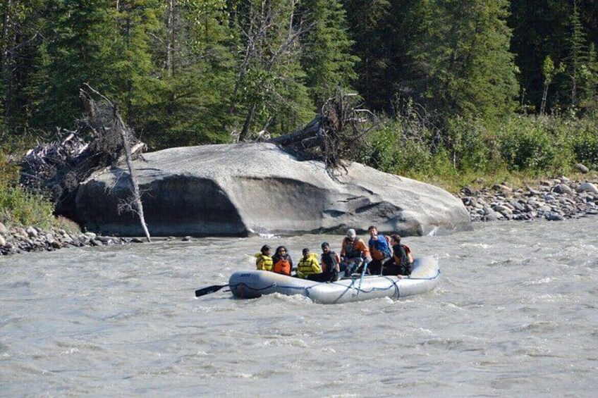 A group of people in a raft navigating a river with a large rock formation in the background. 4