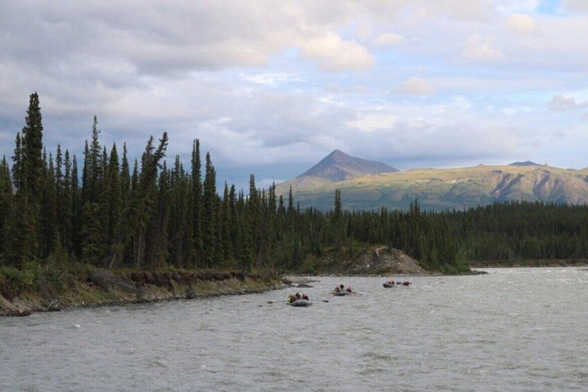 A river with kayaks, dense coniferous forest, and a mountain in the background. 2