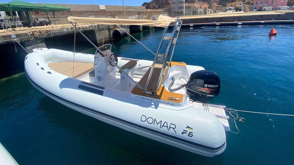 A white motorboat named 'DOMAR F6' docked at a marina with a stone wall and buildings in the background. 5