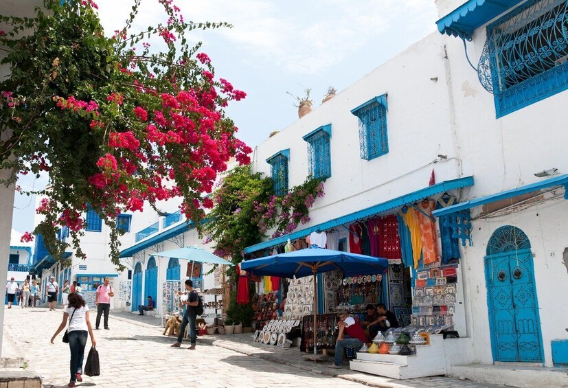 Une rue bordée de bâtiments blancs, de portes bleues et d’une boutique où l’on trouve des articles aux couleurs vives. 3