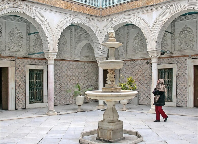 Une cour intérieure avec une fontaine centrale, des arcades décorées et une personne qui se promène. 4