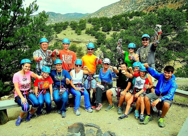 A group of people with helmets and cycling gear, posing on a rocky terrain with trees and hills in the background. 3