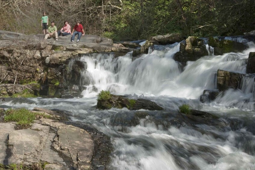 A waterfall cascading over rocks in a forested area with people observing the scene. 4
