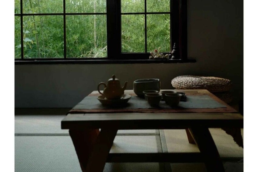 A table with a teapot and cups, a woven basket, and a window with greenery outside. 5