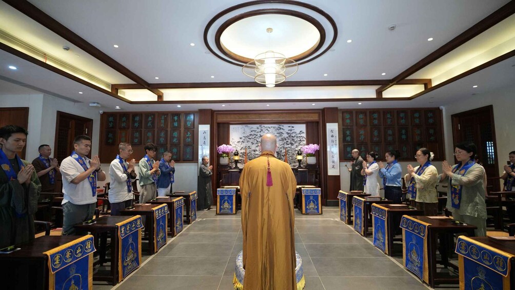 A ceremonial hall with a central figure in traditional attire, attendees in rows, and a chandelier. 3