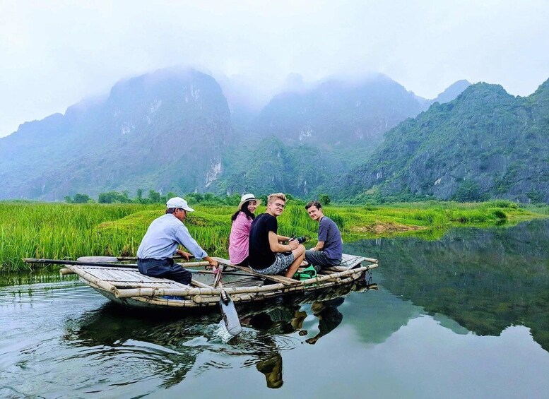 A group of people on a bamboo boat in a calm river with lush greenery and mountains in the background. 3