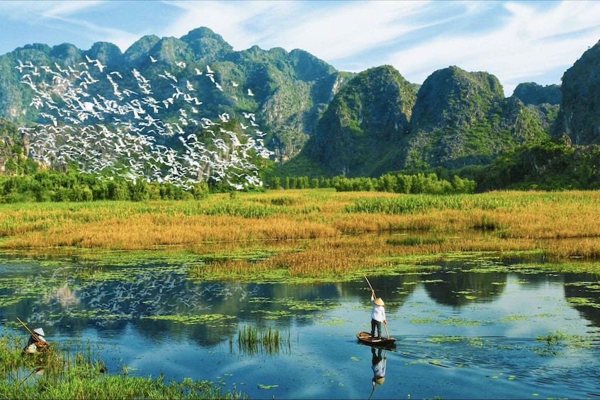 A person standing on a boat in a calm water body surrounded by lush greenery and mountains. 1
