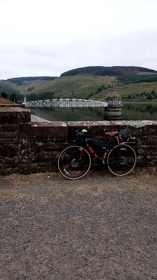 A bicycle parked on a gravel path with a bridge and hills in the background. 2