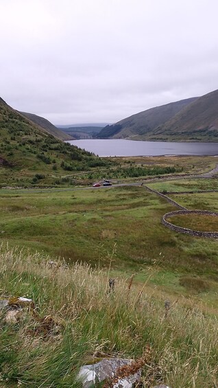 A lake surrounded by hills, a road with vehicles, and a stone wall. 3