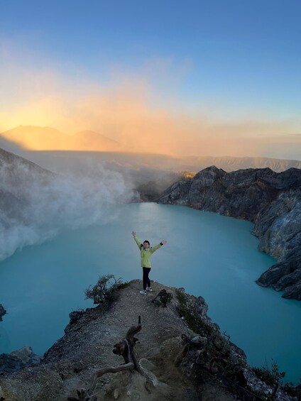 Une personne se tient debout sur un promontoire rocheux, les bras levés, et surplombe un lac turquoise entouré de montagnes. 2