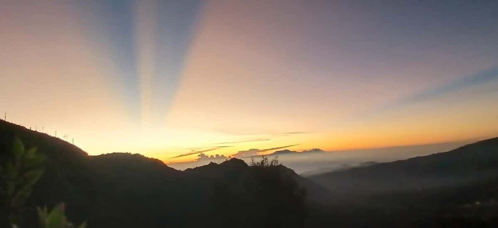 Un lever de soleil sur un paysage montagneux, avec du brouillard et un ciel dégagé. 1