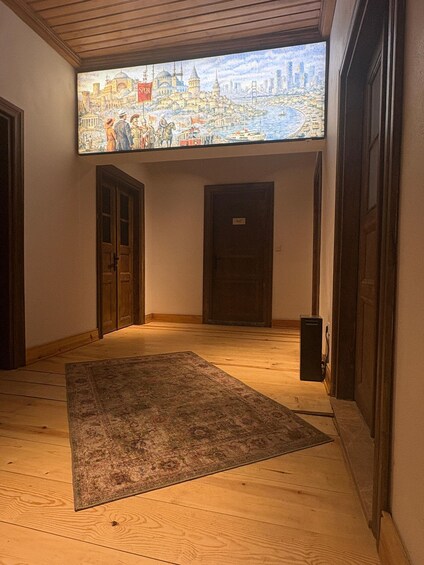 An interior hallway with wooden floors, a rug, and a large window displaying a cityscape. 5