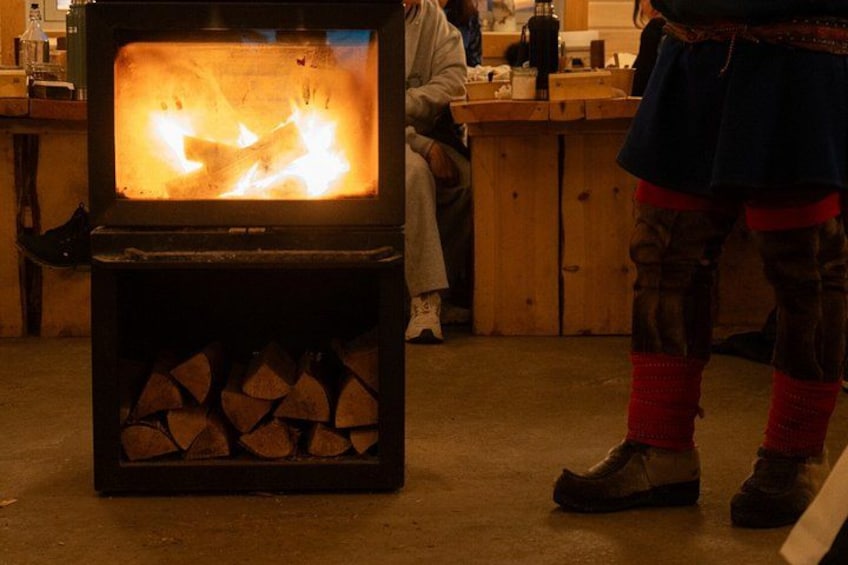 A wood-burning stove with logs inside, a person in traditional attire, and a kitchen setting. 3
