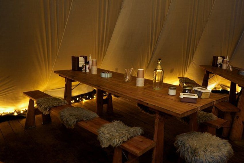 A cozy interior of a tent with a wooden table, benches, and string lights. 5