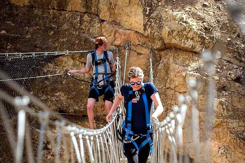 Two people crossing a rope bridge in a rocky canyon. 1