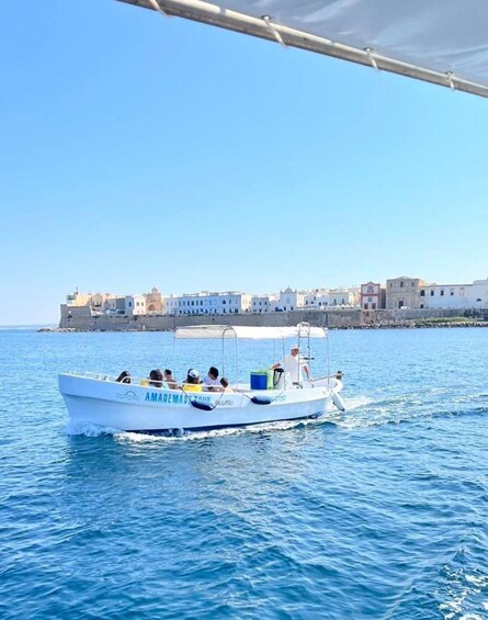 A boat named 'AMAREMARE TOUR' on calm blue waters with a coastal town in the background. 1