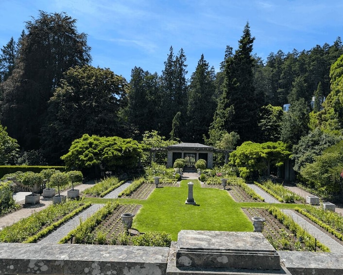 A formal garden with a central gazebo, neatly trimmed hedges, and a variety of trees. 5
