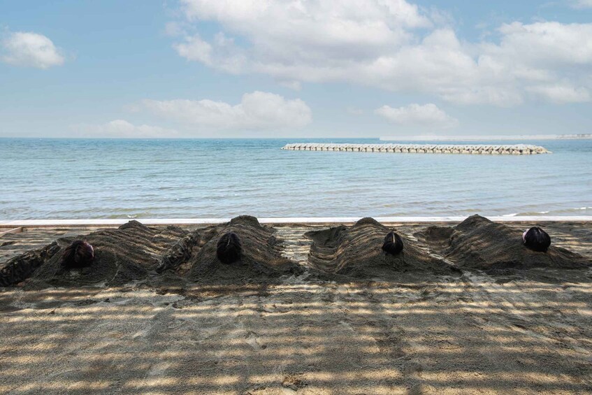 A sandy beach with four large mounds of earth and a breakwater in the distance. 2
