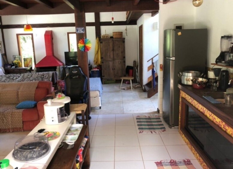 A living room with a sofa, a gaming chair, a table with a fan, and a kitchen area with a refrigerator and stove. 2