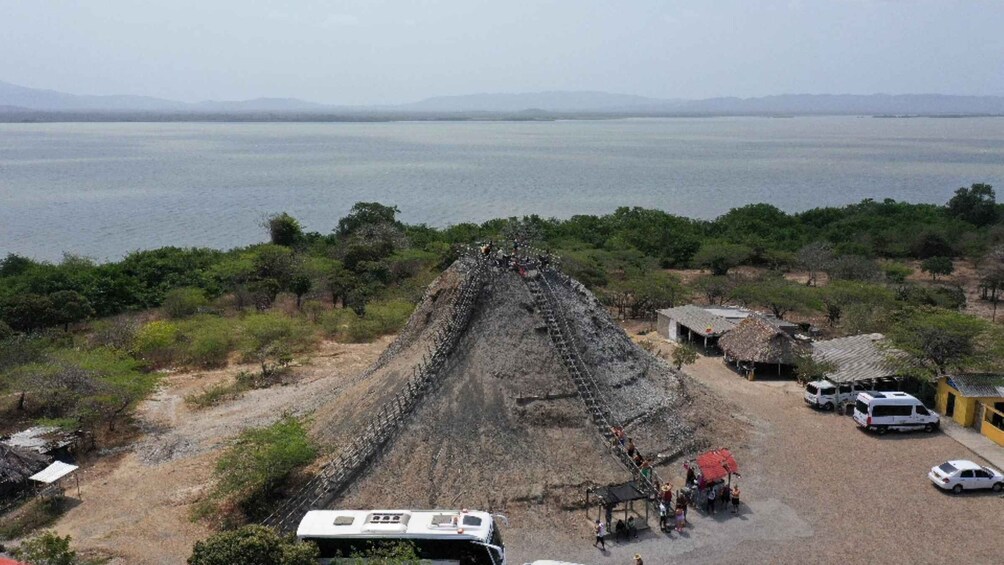 A pyramid structure with people ascending it, surrounded by a rural landscape with trees and a body of water in the background. 5