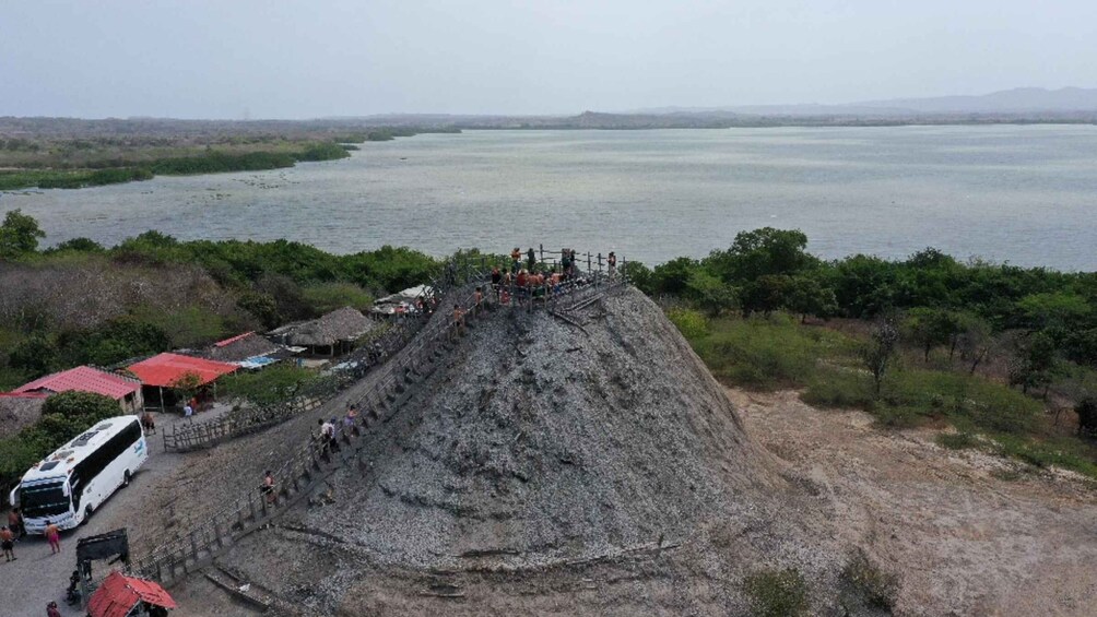 A large earthen mound with people on top, a river in the background, and a bus parked nearby. 2