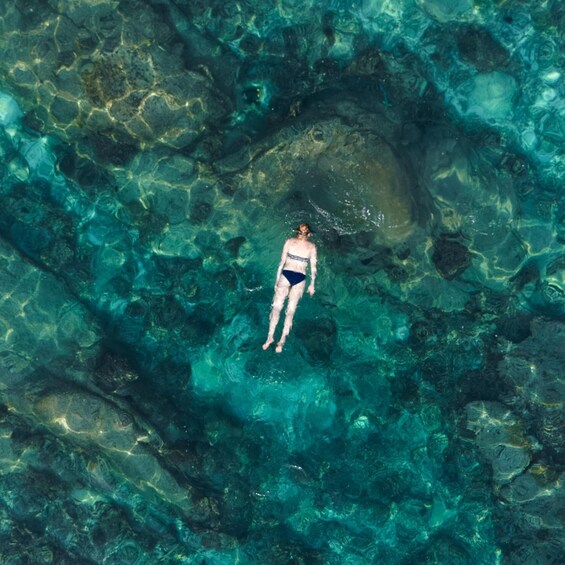 A person swimming in clear blue water surrounded by rocks. 5