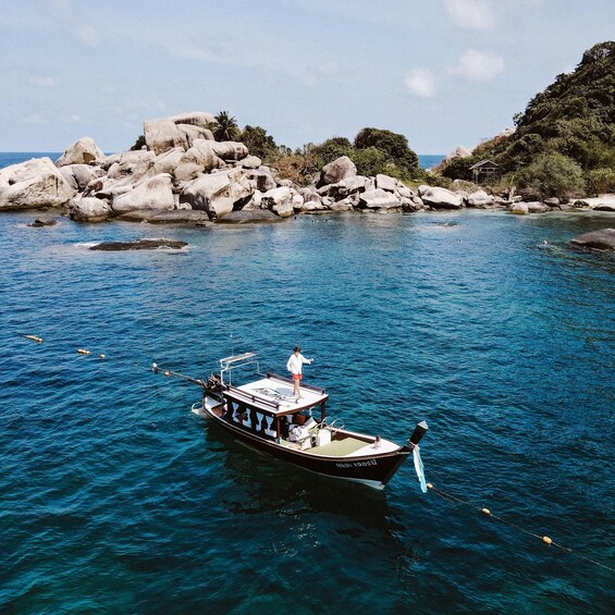 A boat on clear blue water with a rocky shoreline and greenery in the background. 3
