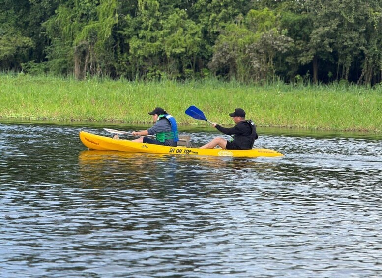 Two people kayaking on a calm river surrounded by greenery. 2
