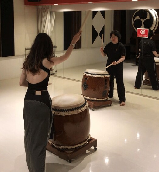 A person playing a drum in a room with a mirror and a no-smoking sign. 5