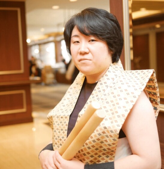 A person holding rolled-up papers in a patterned vest. 3