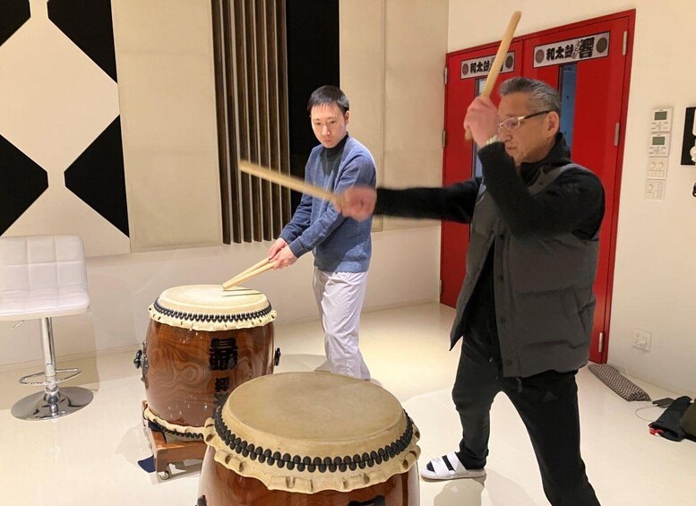 Two individuals playing drums in a room with a modern interior design, including a red door and a white chair. 4