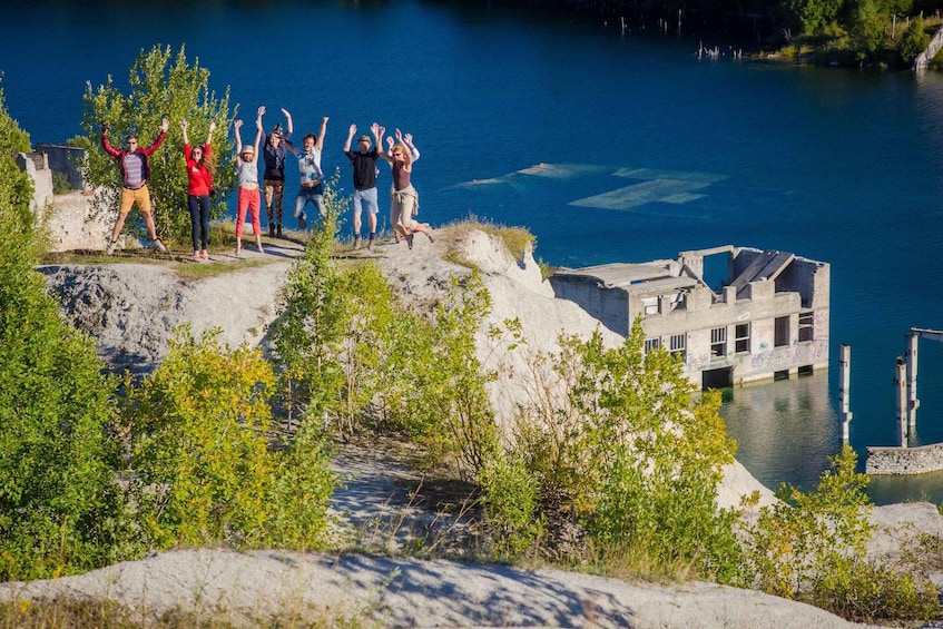 A group of people standing on a cliff overlooking a body of water with a dilapidated building in the background. 4