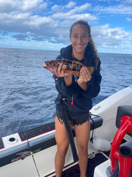 A person holding a fish on a boat with the ocean and sky in the background. 1