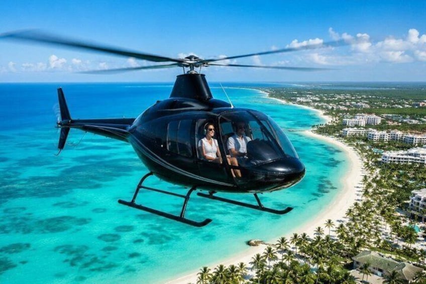 A helicopter over a turquoise beach with palm trees and resort buildings. 1