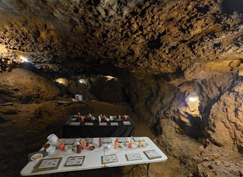 A cave dining area with tables set for a meal, surrounded by rocky walls and illuminated by spotlights. 4