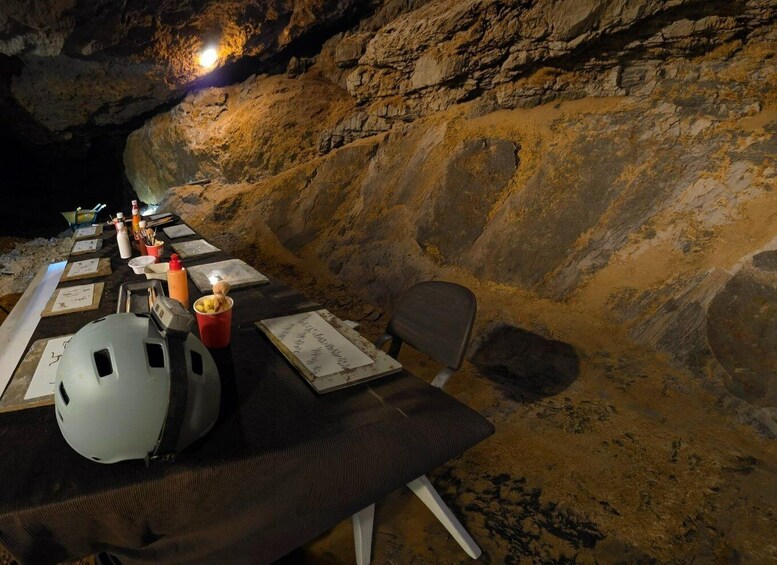 A cave interior with a table set for an event, including a helmet, food containers, and papers. 5