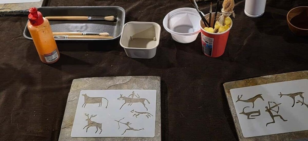 A table with art supplies, including paintbrushes, a paint container, and paper with animal drawings. 1