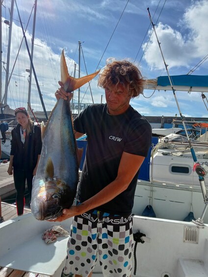 A person holding a large fish on a boat with other boats in the background. 5