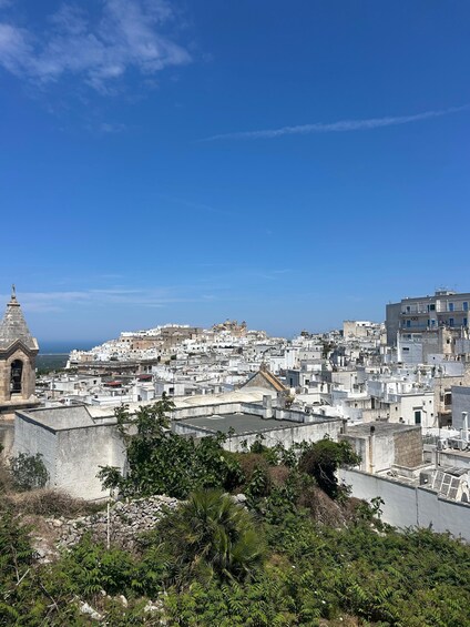 A coastal cityscape with dense white buildings, a prominent church with a bell tower, and a clear blue sky. 4