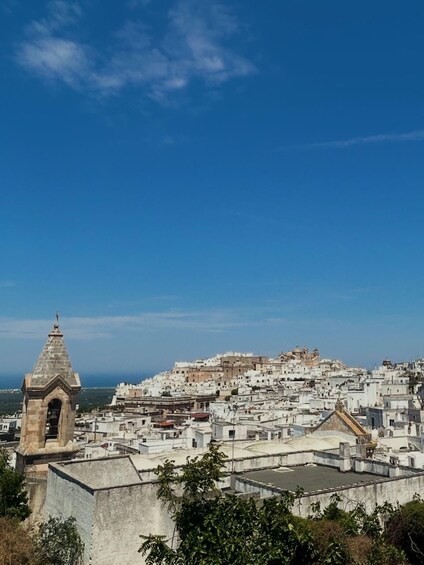 A coastal cityscape with white buildings, a prominent tower, and a clear blue sky. 2
