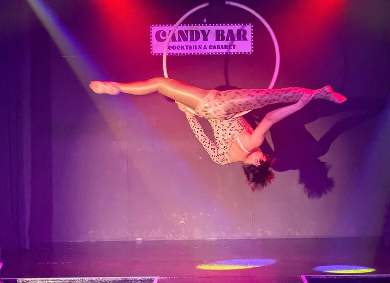 A person performing an aerial act at a venue with a sign reading 'CANDY BAR COCKTAILS & CABARET'. 3