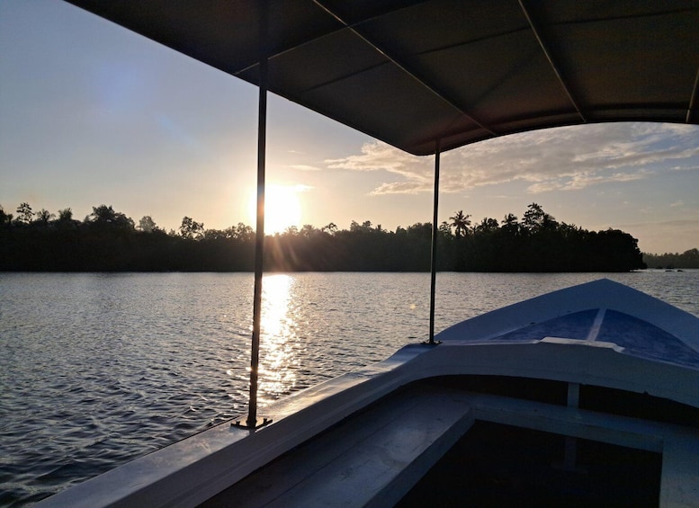 A boat on calm water with a sunset in the background and a forested shoreline. 2