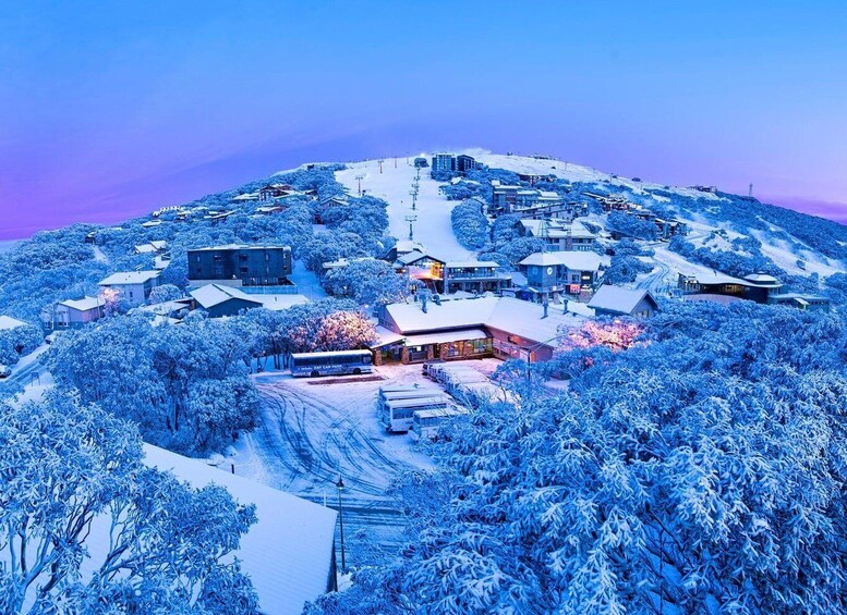 A snow-covered mountain town with buildings, a bus, and a ski lift. 2