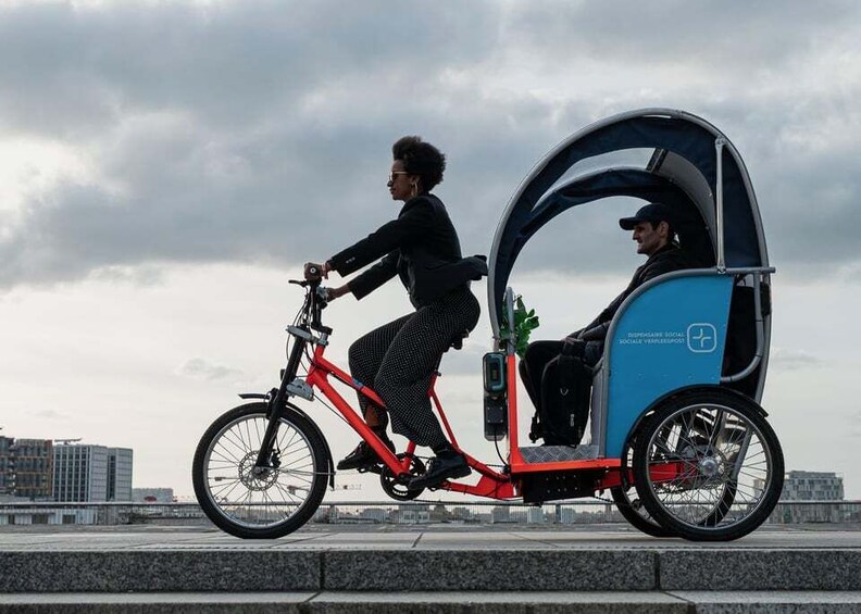 A person riding a red bicycle with a blue tricycle attached, on a bridge with a city skyline in the background. 5
