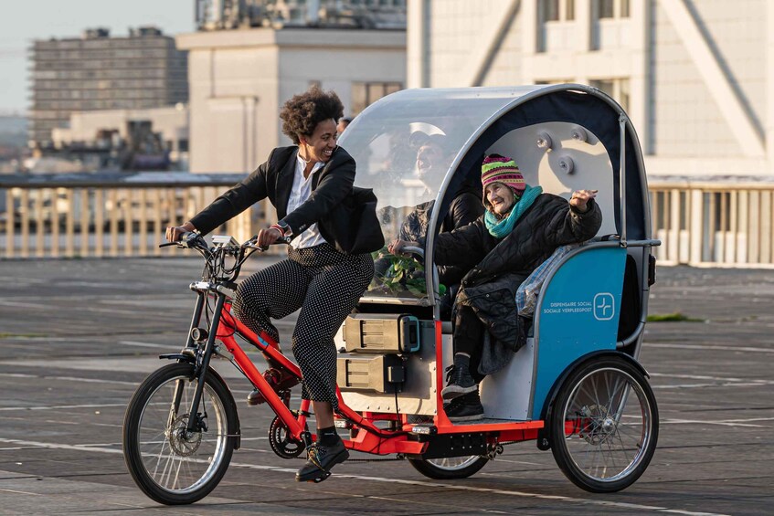 A person riding a bicycle with a cargo box attached, and another person sitting in a covered vehicle. 2