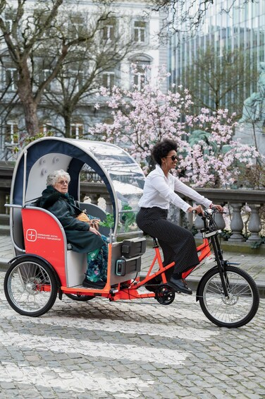 A person riding a red bicycle with a covered seat, another person seated in the covered area, and cherry blossoms in the background. 1