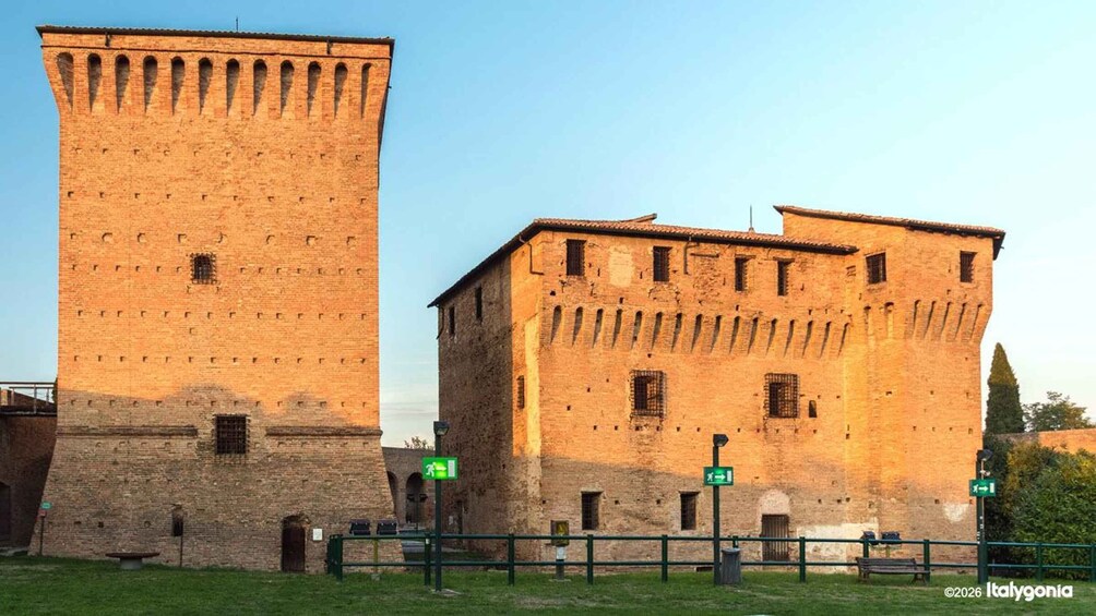 A historic brick tower and a building with a sloped roof, both featuring arched windows and a brick facade. 1