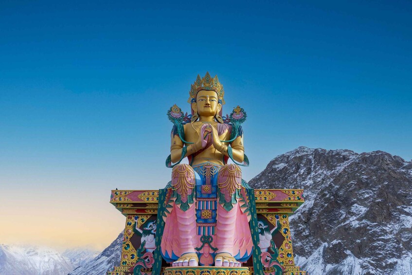 A large, colorful statue of a deity with intricate patterns, set against a backdrop of snow-capped mountains and a clear sky. 5