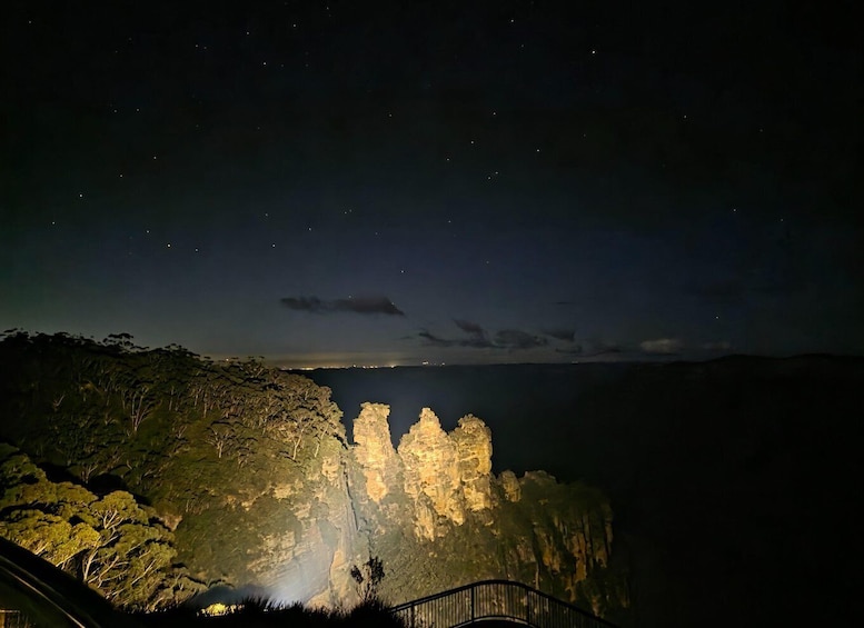 A night view of a cliff with illuminated rock formations and a distant city skyline. 1